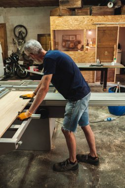Bir marangozun endüstriyel kesim makinesindeki büyük tahta parçalarını tutarken yandan görünüşü
