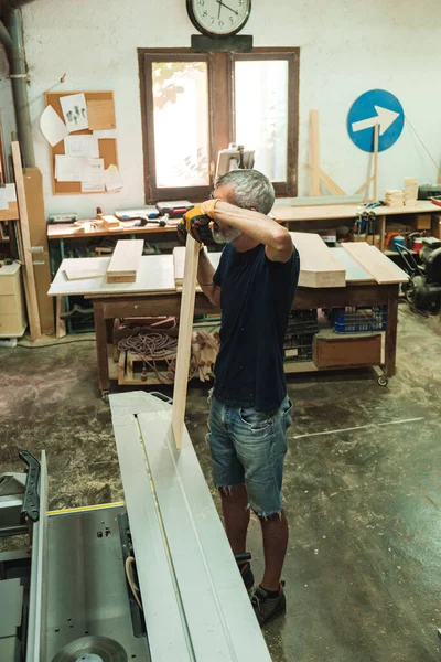 Marangoz bir tahta parçasını ahşap atölyesinde mezura ile ölçüyor.