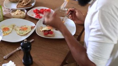 Uzun kollu beyaz bir gömlek ve bilezik giyen bir kişi dilimlenmiş domateslerle bir yemeği hazırlarken veya yerken ahşap bir masada oturur. 25 saniye.