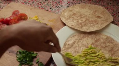 Avokado, doğranmış yeşillikler ve tortilla dürümleriyle taco hazırlayan insanların 15 saniyelik videosu..
