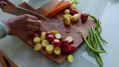 Ahşap doğrama tahtasındaki sebzeleri hazırlayan insan elleri