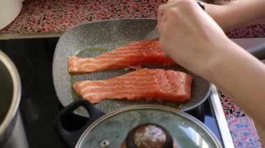 Close up of person frying salmon fish on electric stove               