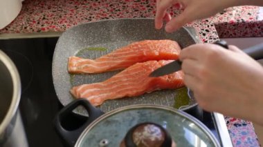 Close up of person frying salmon fish on electric stove               