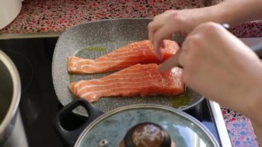 Close up of person frying salmon fish on electric stove               