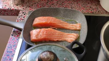 Close up of person frying salmon fish on electric stove               