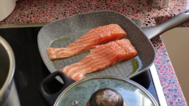 Close up of person frying salmon fish on electric stove               