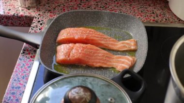 Close up of person frying salmon fish on electric stove               