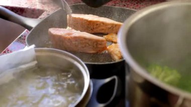 Close up of person frying salmon fish on electric stove               