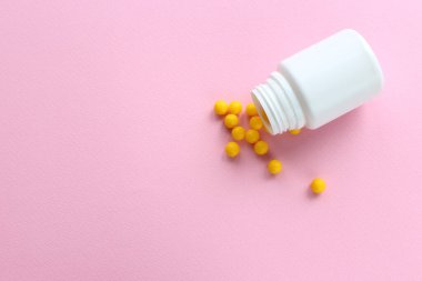 Sarı vitaminler pembe arka plana saçılmış.
