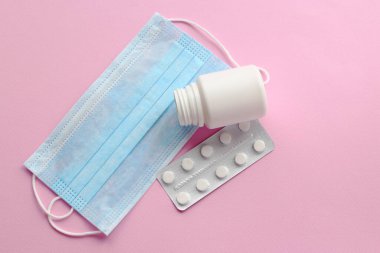 Tek kullanımlık mavi maskeler ve açık pembe arka planda haplar.