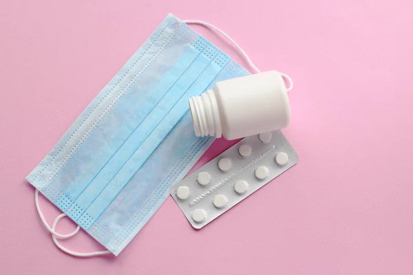 Tek kullanımlık mavi maskeler ve açık pembe arka planda haplar.