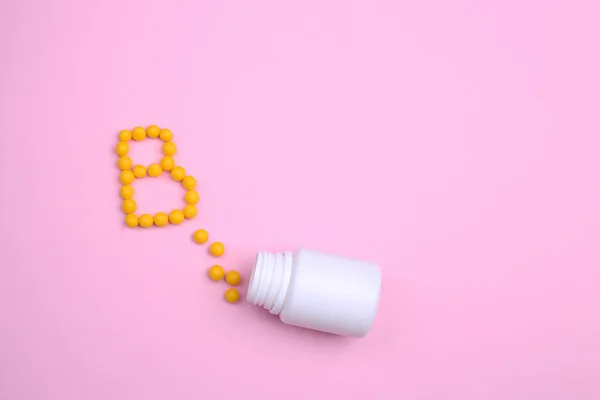 Vitaminler, B harfi gibi pembe bir zemin üzerine saçılmıştır.