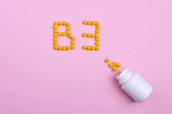 Vitaminler pembe bir zemin üzerine dağılmış, tıpkı B3 harfi gibi.