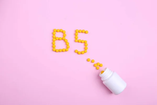 Vitaminler, B5 harfi gibi pembe bir zemin üzerine saçılmıştır.
