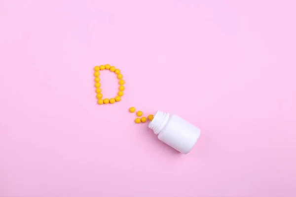 Yaratıcı sağlık ve tıp konsepti D harfi gibi pembe bir zemin üzerinde vitamin ve kapsüller.