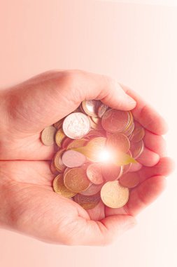 Erkeklerin elinde sikkeler, para tasarrufu kavramı ve madeni paralarda turuncu ışık ile altın fon tasarrufu.