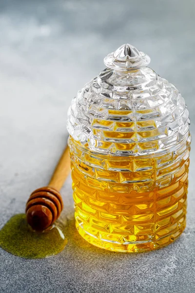 Liquid flower honey in a glass jar with wooden honey dipper