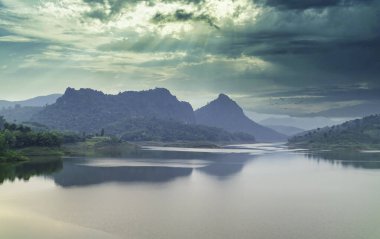 Karmaşık dağların arasından akan nehrin güzel manzarası. Güneş güzel yağmur bulutlarının arasından parladığı zaman..