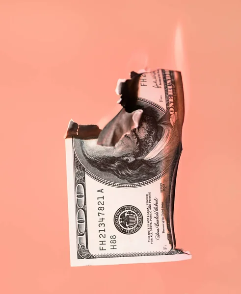 Burning hundred dollars cash on orange background