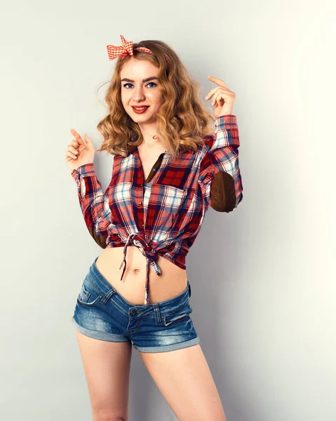 Девушка с кудрявыми светлыми волосами с красным клетчатым бантом и рубашкой в джинсовых шортах. — стоковое фото