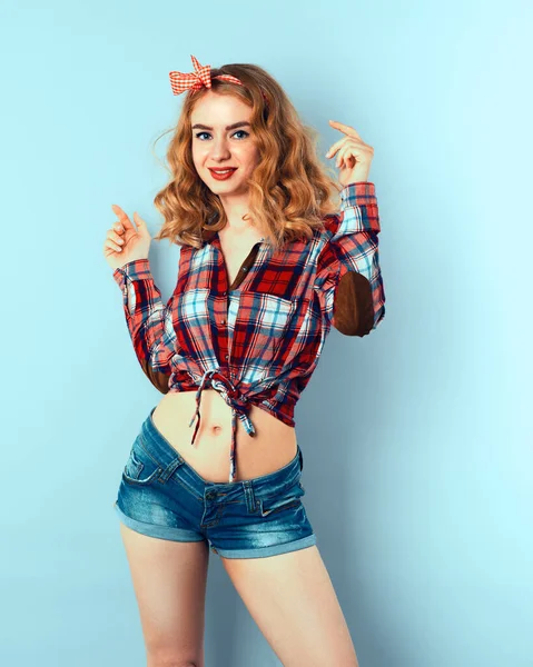 Pin-up Mädchen mit lockigem blondem Haar mit rot karierter Schleife und Hemd in Jeans-Shorts. — Stockfoto