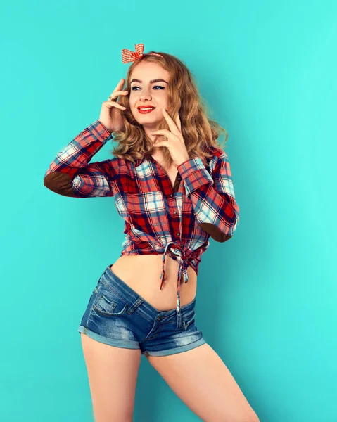 Pin-up chica con el pelo rubio rizado con rojo arco a cuadros y camisa con pantalones vaqueros cortos. —  Fotos de Stock