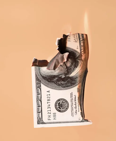 Spalování sto dolarů v hotovosti na světle oranžovém pozadí — Stock fotografie