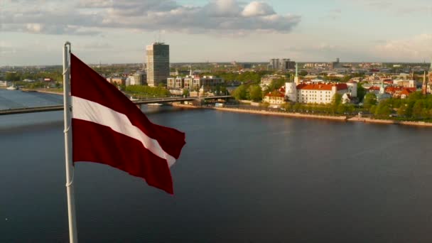 Bandera letona ondeando en el viento con una ciudad riga — Vídeo de stock
