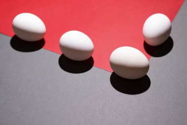 Gri arkaplandaki kırmızı üçgenin kenarındaki beyaz yumurtalar.