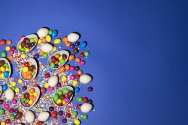 Çikolatalı yumurtaların, renkli jölelerin ve tatlı tozların yarıları mavi arka planda uzanıyor.