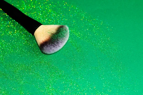 Een borstel voor poeder met groene glitters op een glanzende groene achtergrond — Stockfoto