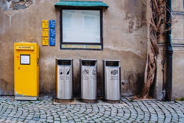 On a street there are 3 green recycling bins on a hedge. Translation: 