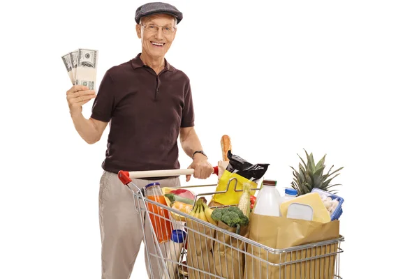 Sénior posando com carrinho de compras e pacotes de dinheiro — Fotografia de Stock