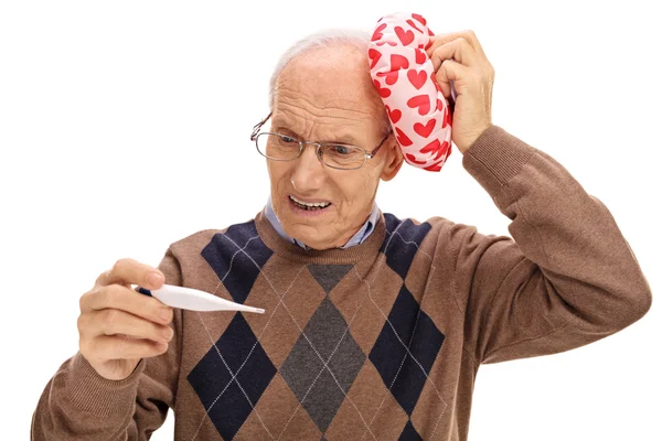 Senior schaut auf Thermometer und hält Eisbeutel in der Hand — Stockfoto