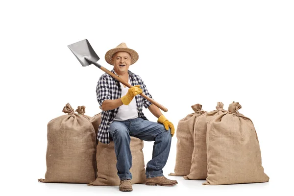 Agricultor sentado en un saco de arpillera y sosteniendo una pala — Foto de Stock