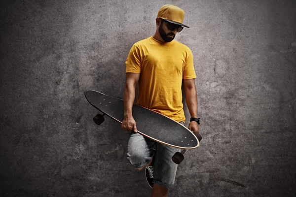 Skater holding longboard en leunend tegen muur — Stockfoto