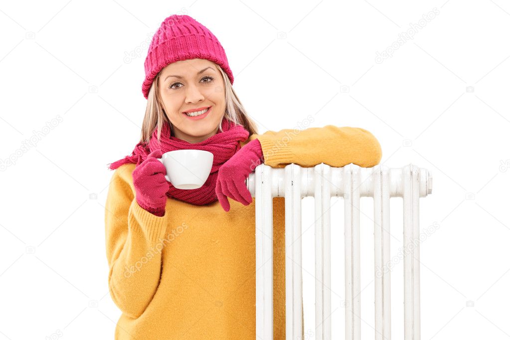 Joyful woman leaning on a radiator and holding a cup