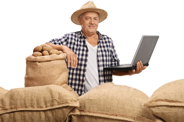 Mature farmer posing with pile of burlap sacks and laptop — ストック写真