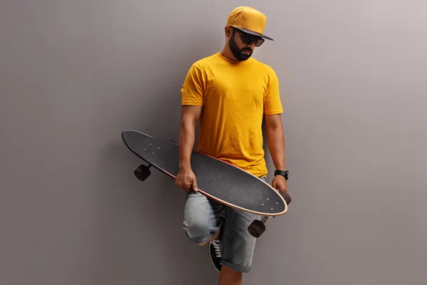 Ragazzo che tiene il longboard e appoggiato al muro — Foto Stock