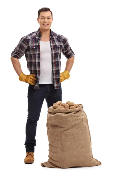 Joven agricultor parado detrás del saco de arpillera lleno de papas — Foto de Stock