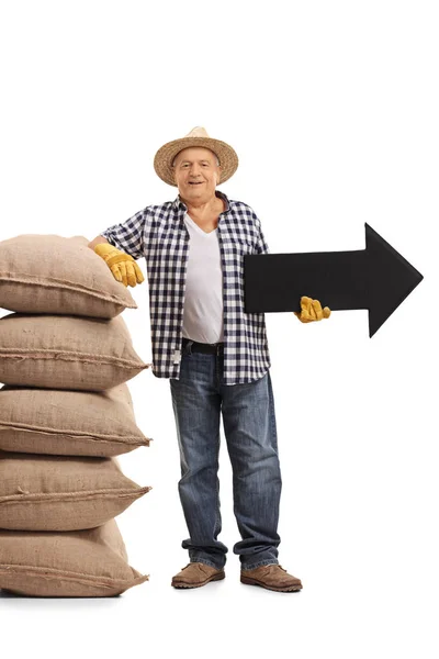 Farmer leaning on pile of burlap sacks and holding an arrow pointing — Stock Photo, Image