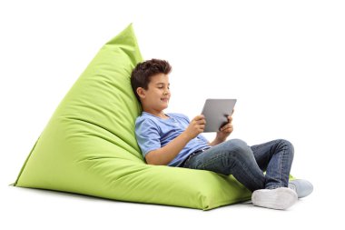 bir puf üzerinde oturan ve bir tablet vasıl arayan çocuk