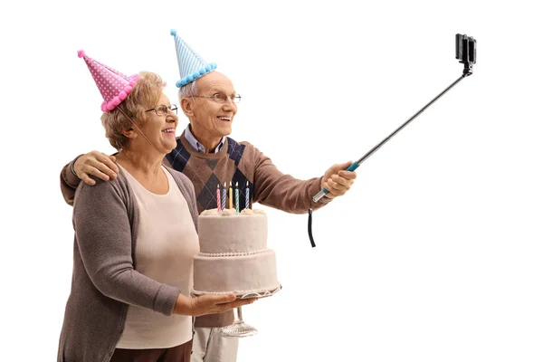 ผู้สูงอายุที่มีหมวกปาร์ตี้และเค้กวันเกิดถ่ายเซลฟี่ — ภาพถ่ายสต็อก