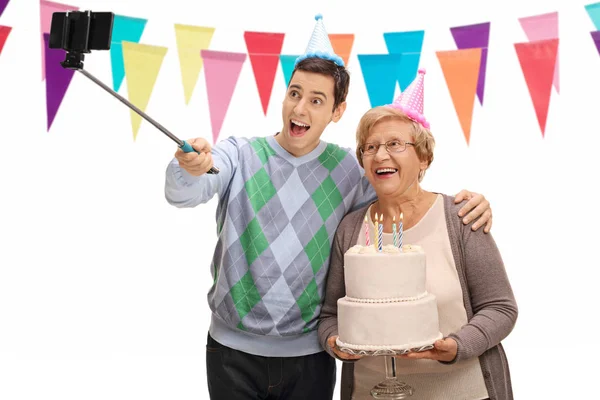 Człowiek i Starsza kobieta z urodzinowego tortu biorąc selfie — Zdjęcie stockowe