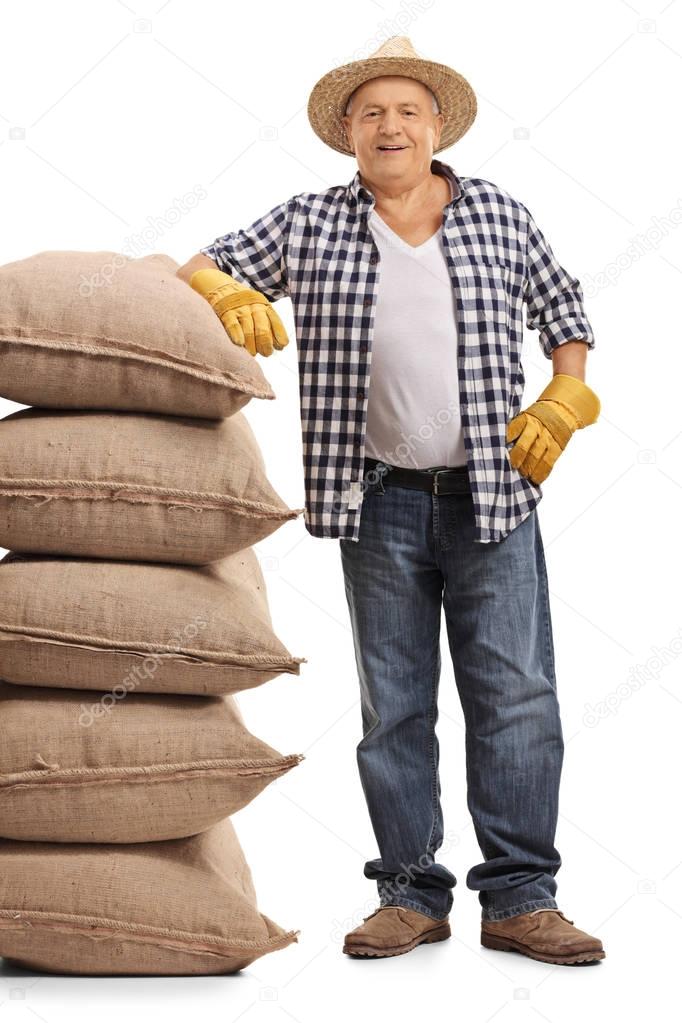 Mature farmer leaning on a pile of burlap sacks