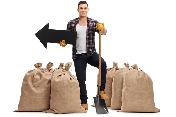 Farmer standing between burlap sacks with shovel and arrow — Stock Photo, Image