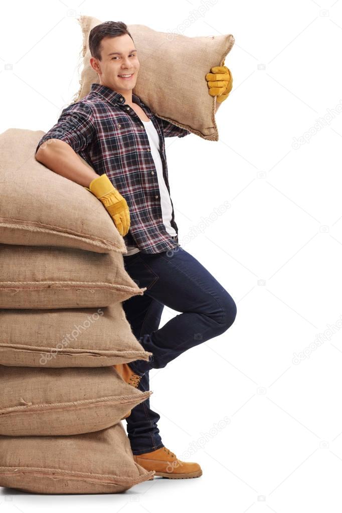 Agricultural worker with burlap sack leaning on stack of burlap 