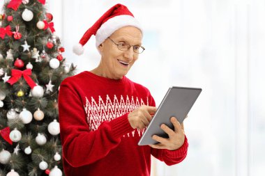 Yaşlı adam tablet Noel ağacı önünde bakarak