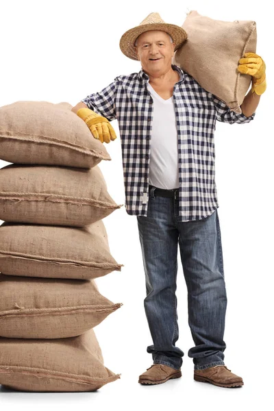 Farmář drží pytli a opírá se o hromadu pytlovina — Stock fotografie