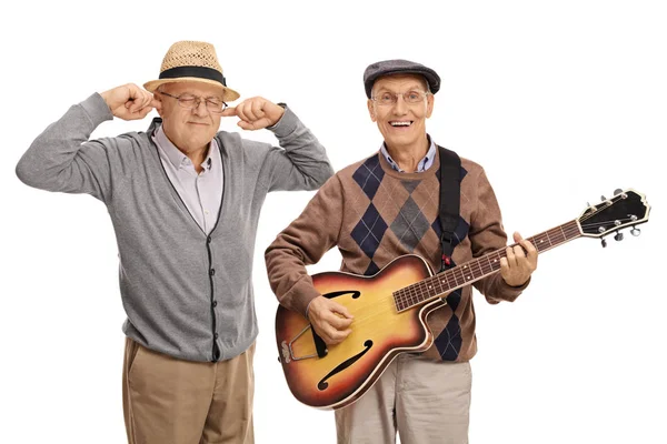 Man playing a guitar with another man plugging his ears — Stock Photo, Image